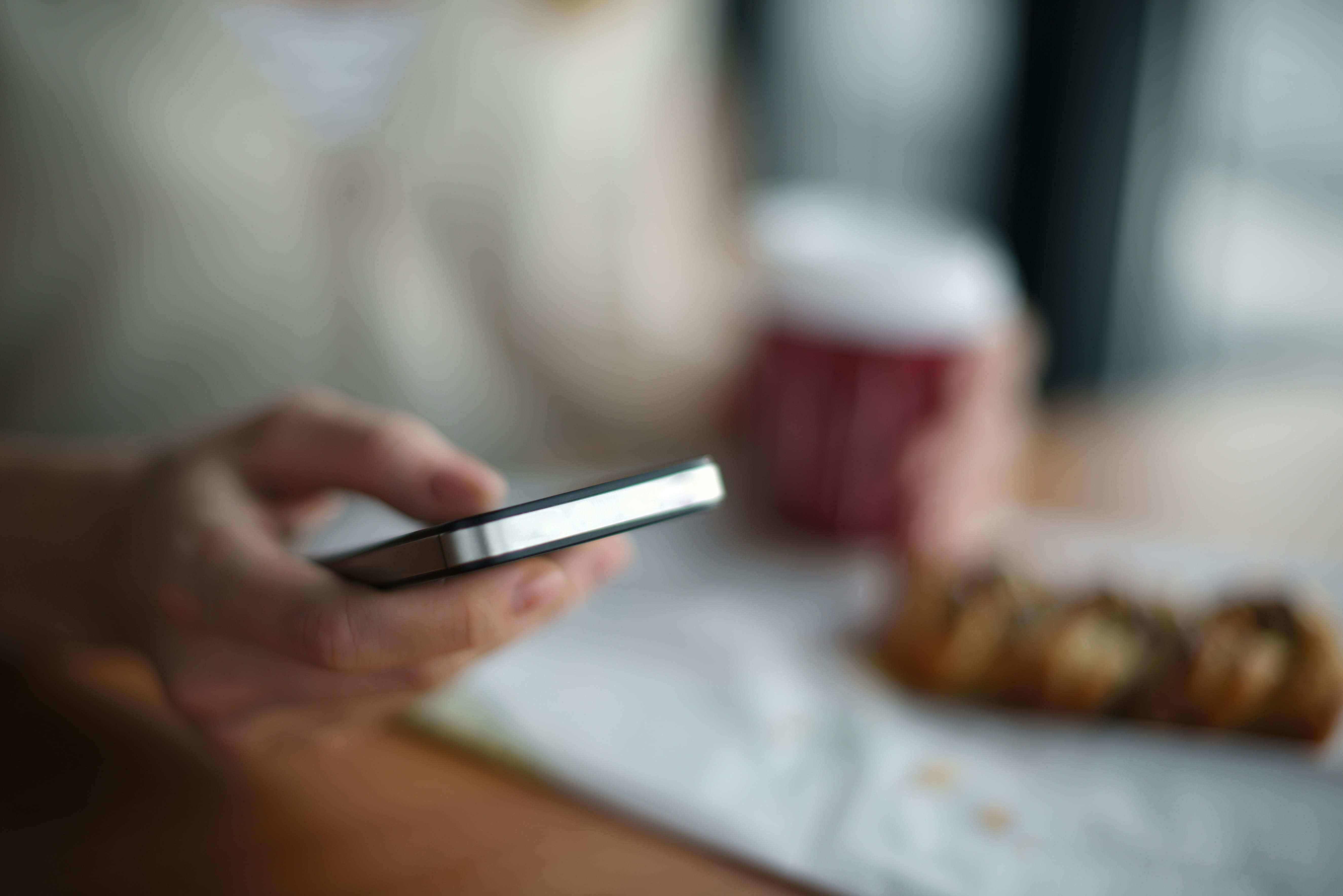 Person checking a booking on their smartphone at a cafe table with a takeaway coffee cup